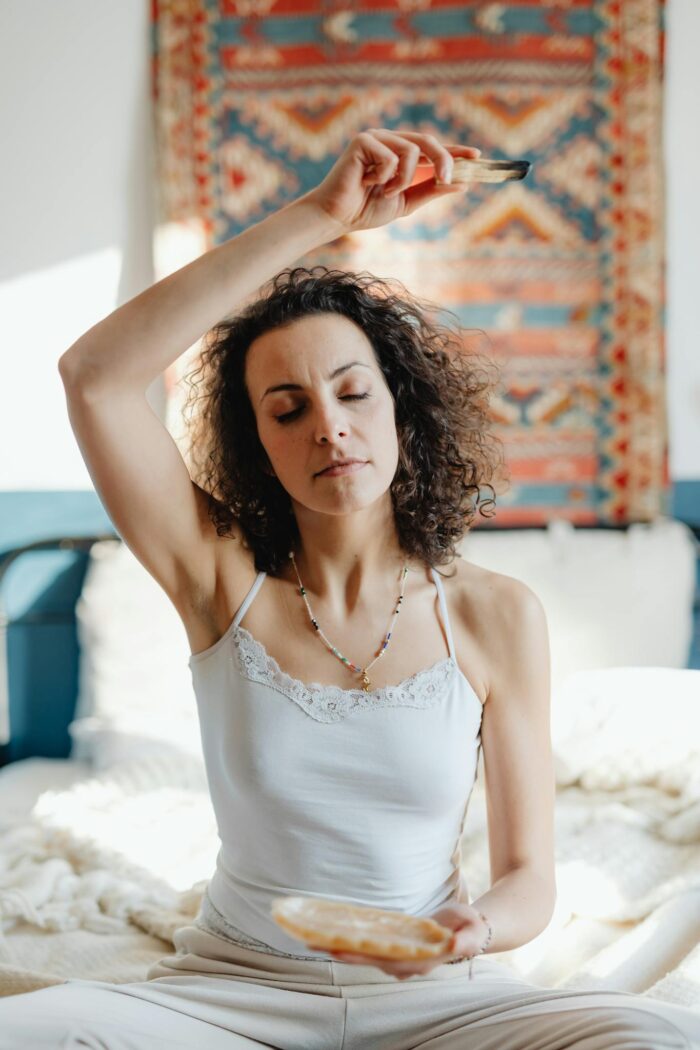 A woman meditates with Palo Santo and crystals in a serene setting, embracing spirituality and relaxation.