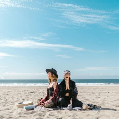 Women practicing meditation and crystal healing on a sunny beach.